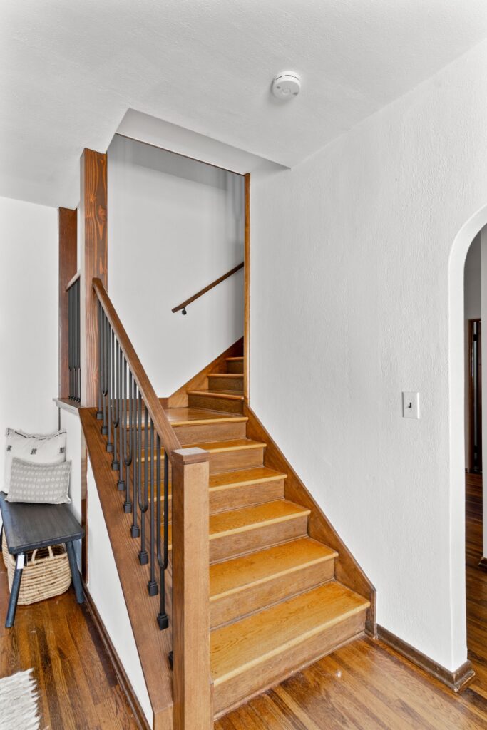 Wood staircase with black metal balusters, stained trim, hardwood flooring and adjacent arched doorway