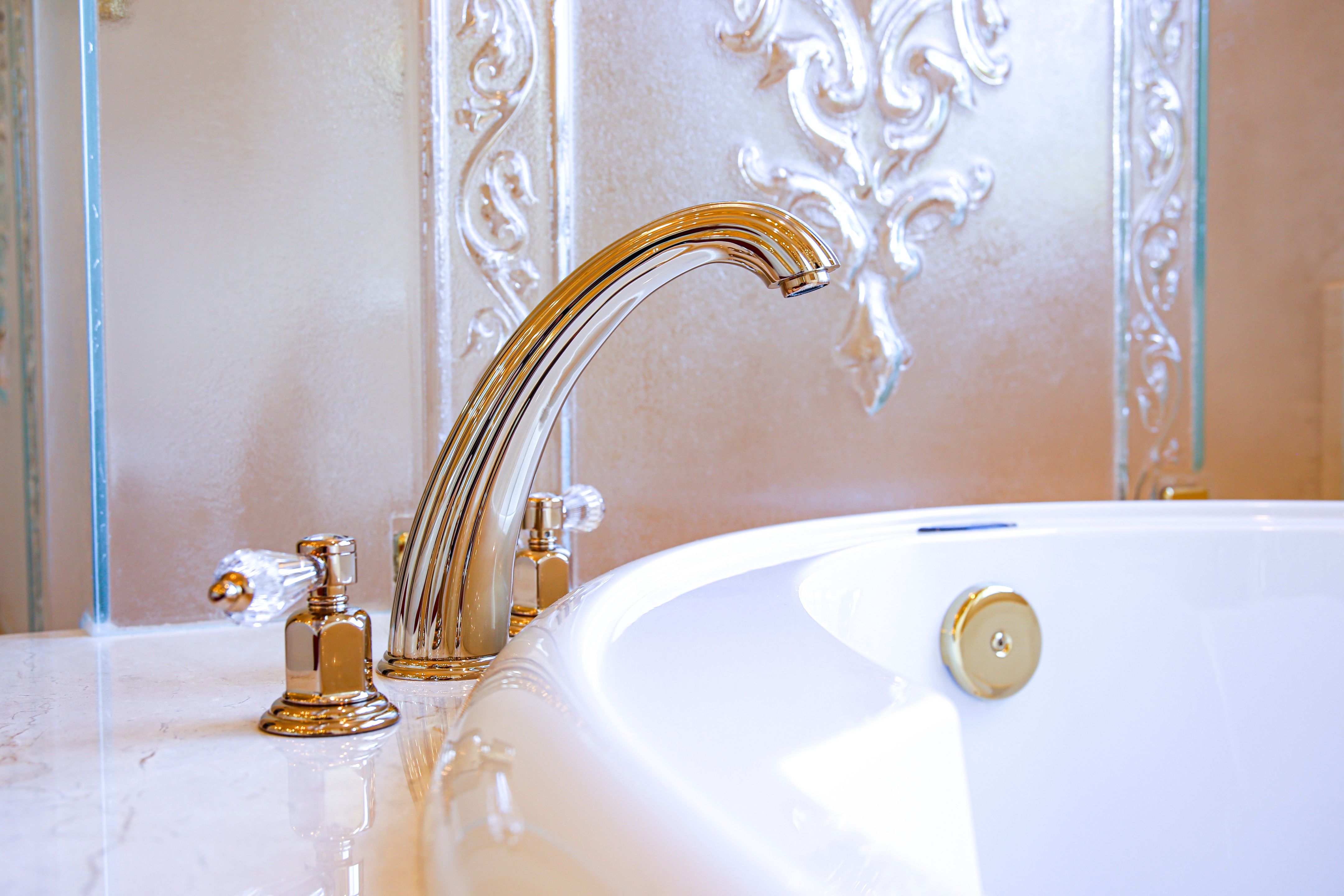 French-gold tub faucet with crystal handles beside the reused soaking tub and ornate molded surround.
