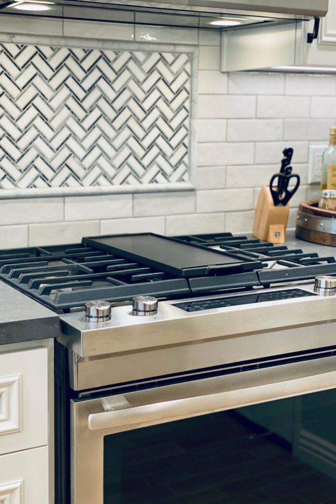 Stainless gas range with cast-iron grates, center griddle and black-and-white herringbone tile backsplash