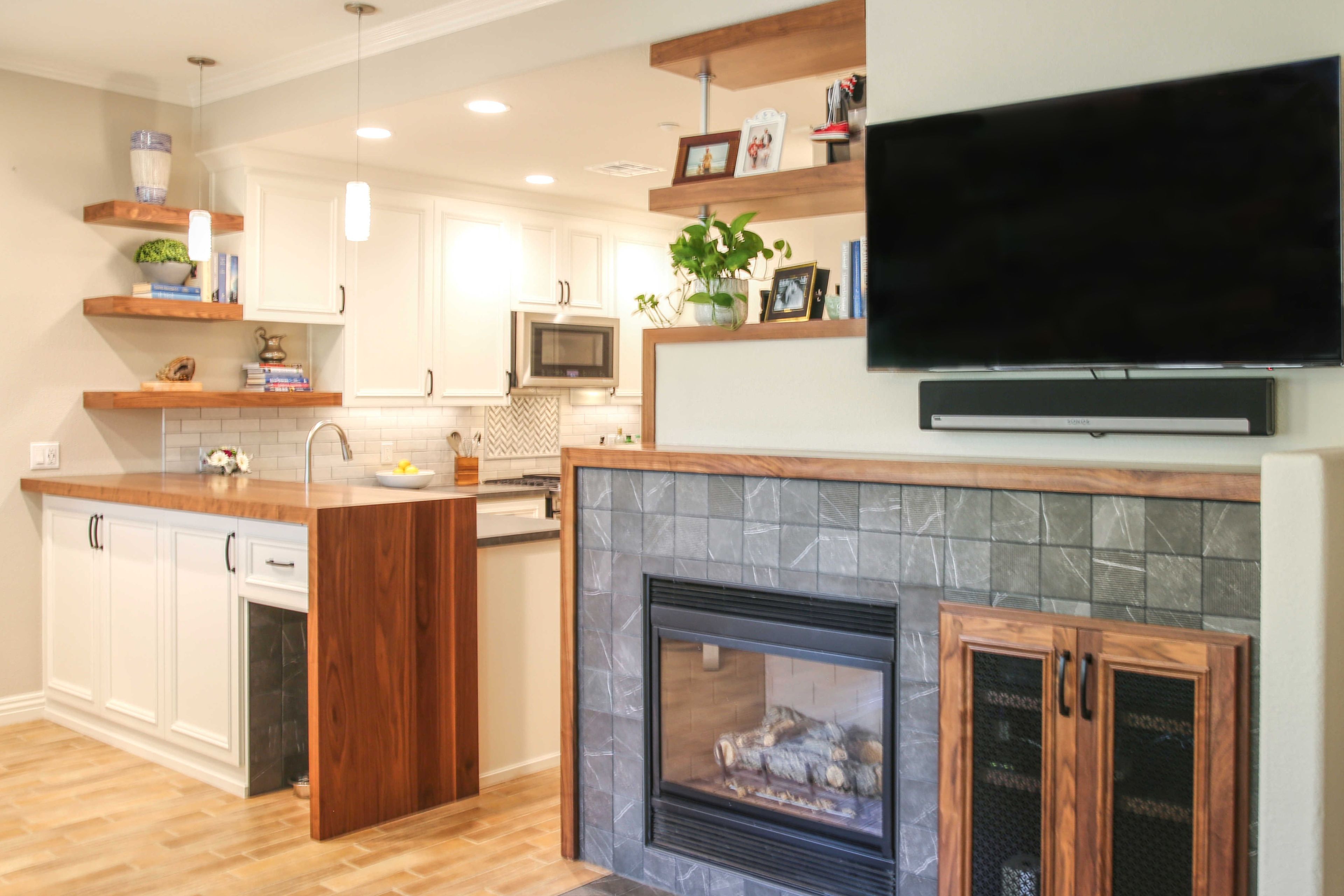 Open kitchen and living area with white cabinetry, wood peninsula, floating shelves and tiled fireplace wall