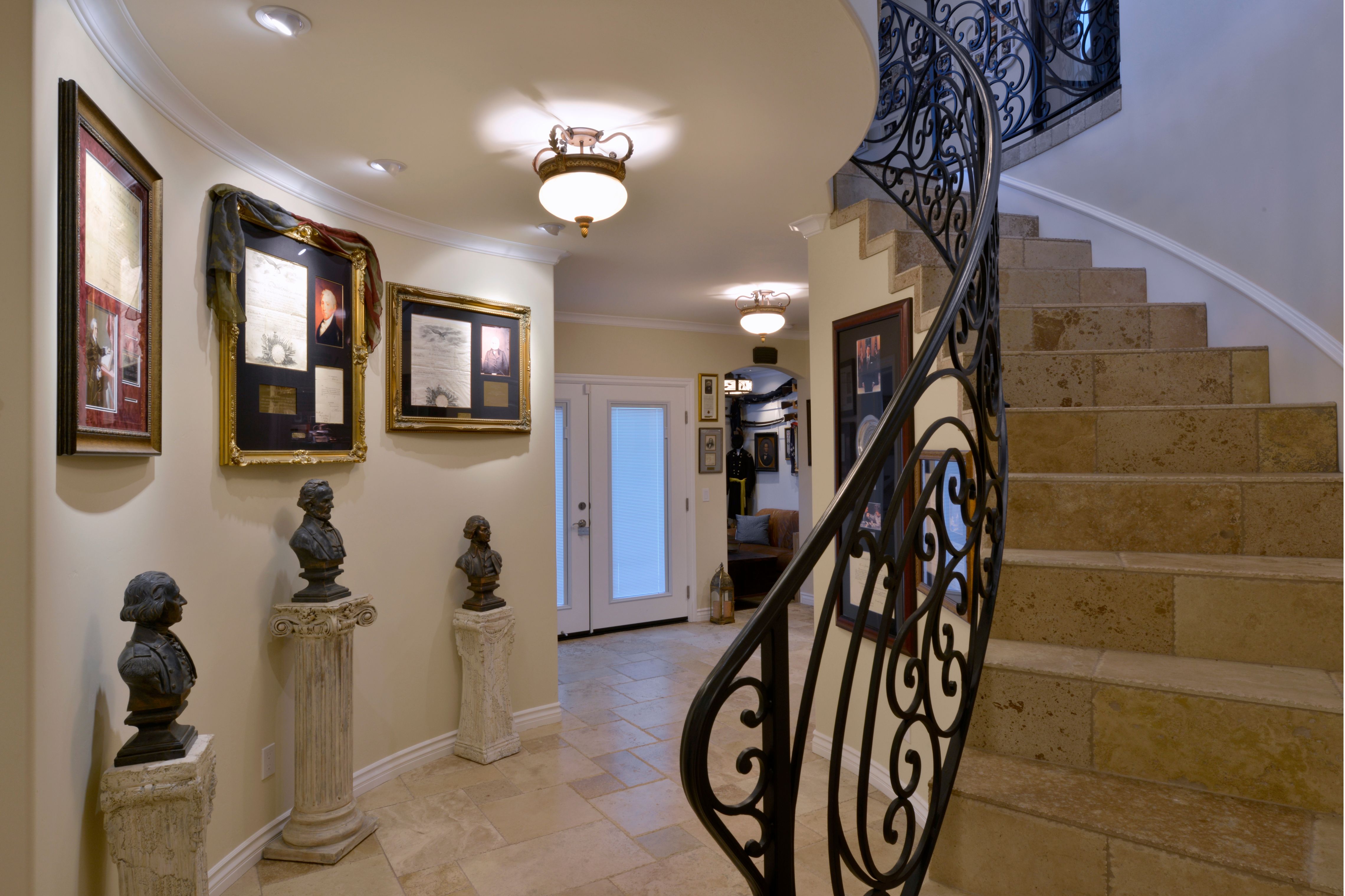 Curved staircase with stone treads, wrought iron railing, tiled entry floor and framed display walls.