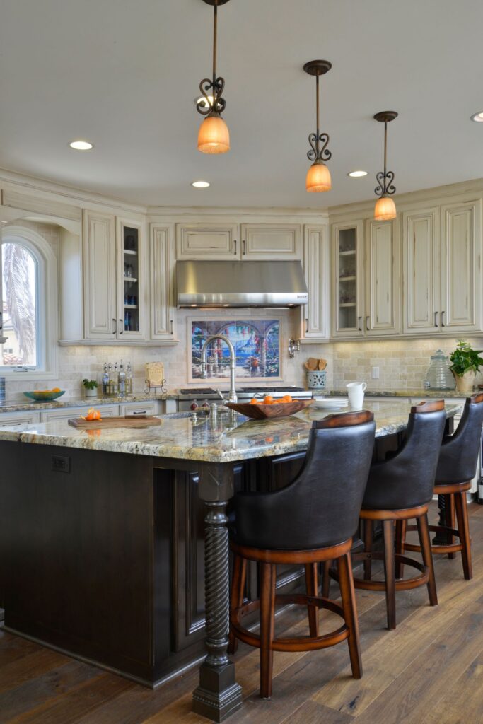 Kitchen with large dark wood island, granite countertop, bar seating, pendant lights and cream cabinetry.