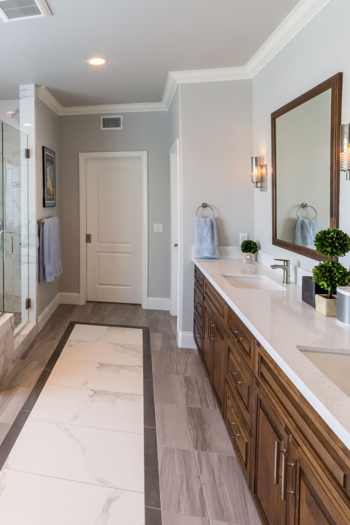 Primary bathroom vanity with wood cabinetry, white countertop, large mirror, sconces and patterned tile flooring.