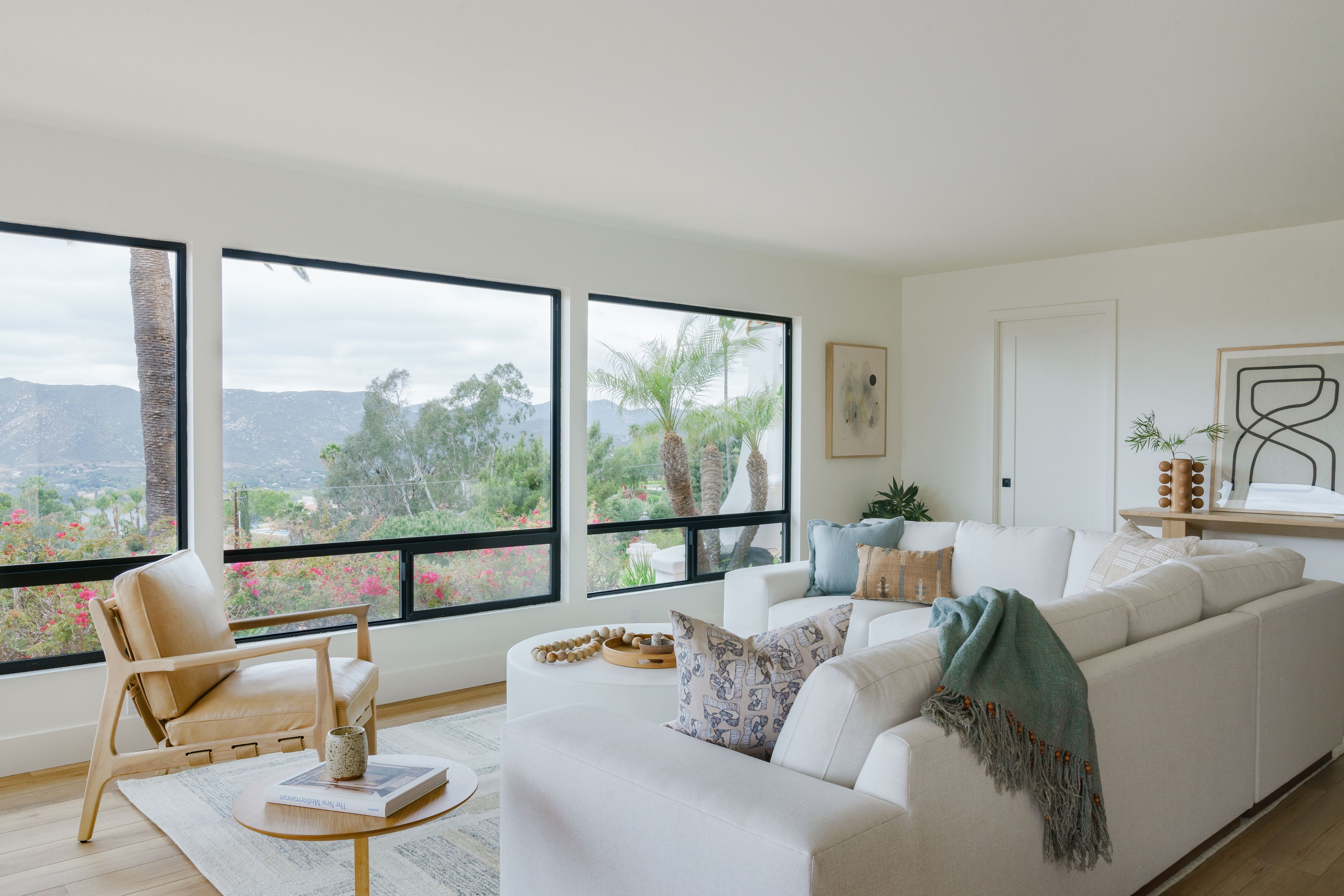 Modern living room with large dark-framed windows, mountain views and neutral upholstered seating