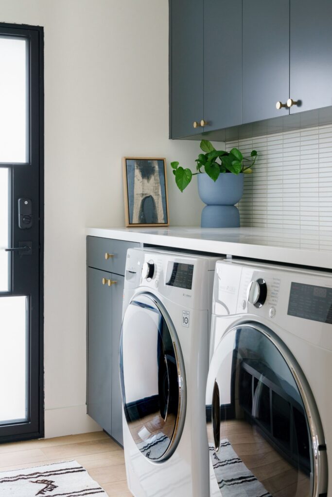 Laundry room with blue cabinetry, white countertop, front-load washer and dryer and black-framed glass door