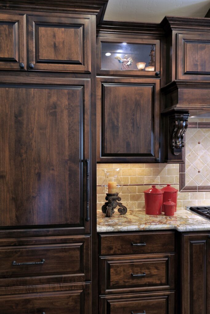 Tall dark wood kitchen cabinetry with lit glass display cabinet, granite counter and under-cabinet lighting