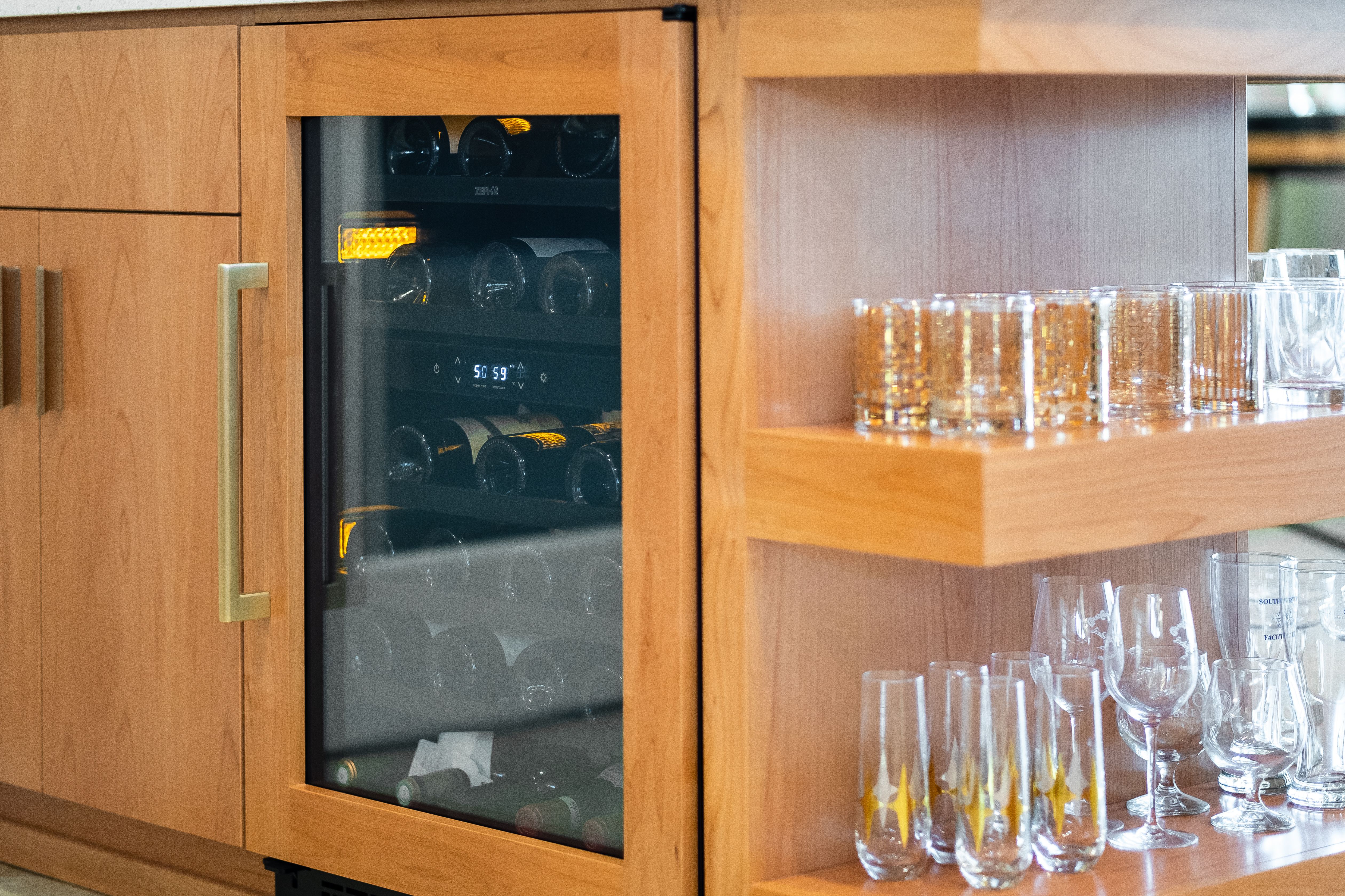 Built-in wine refrigerator with light wood cabinetry and open shelving for glassware