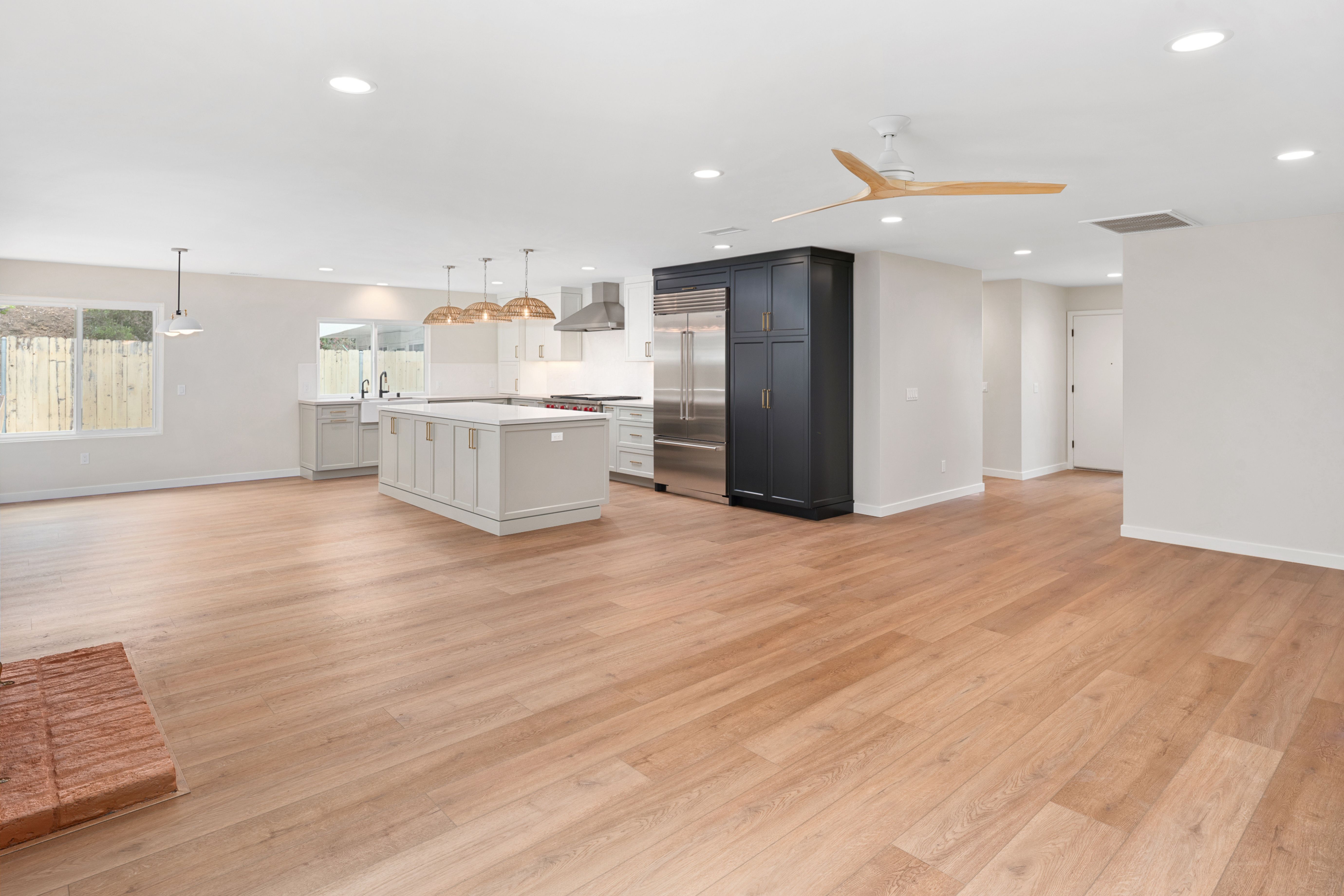 Open-plan kitchen and living area with central island, wood-look flooring, recessed lighting and black pantry cabinetry.