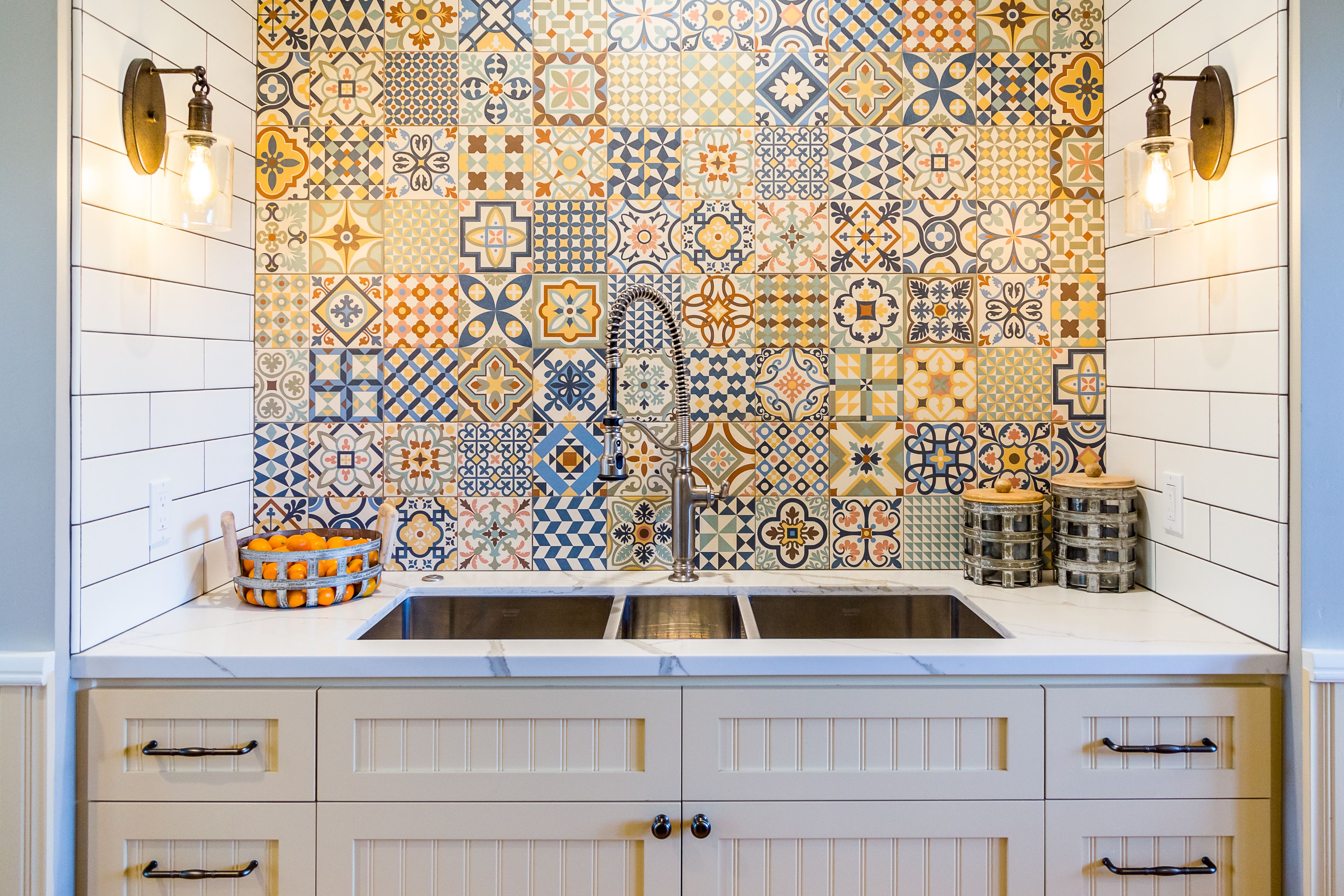 Kitchen sink with colorful patterned tile backsplash, stainless double basin, spring faucet and wall sconces