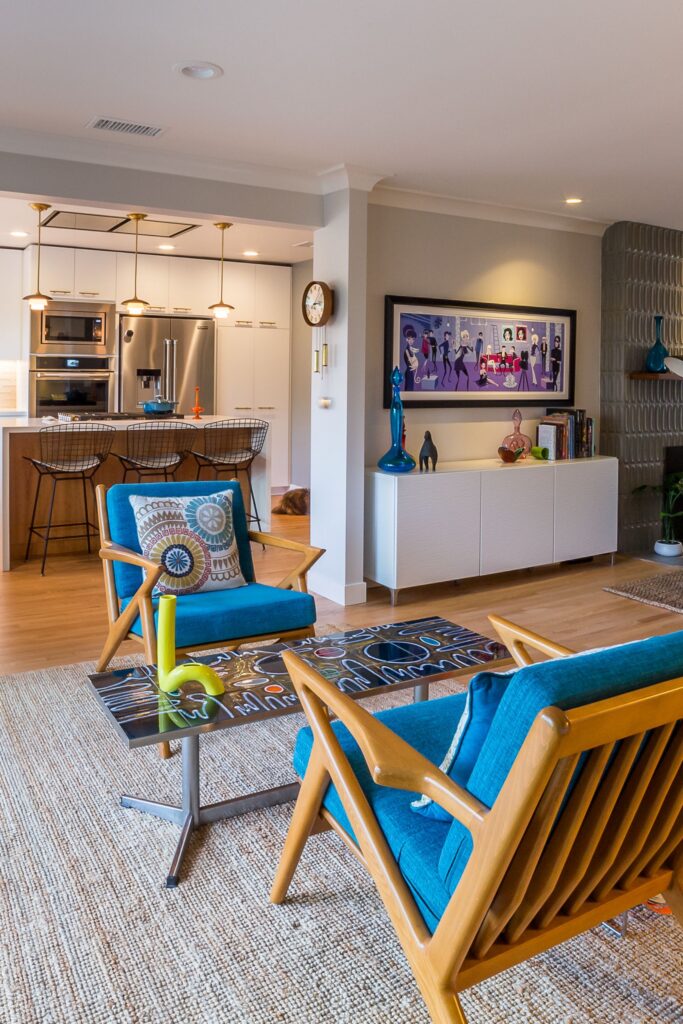 Open living room and kitchen with blue lounge chairs, wood flooring, built-in cabinetry and textured fireplace wall