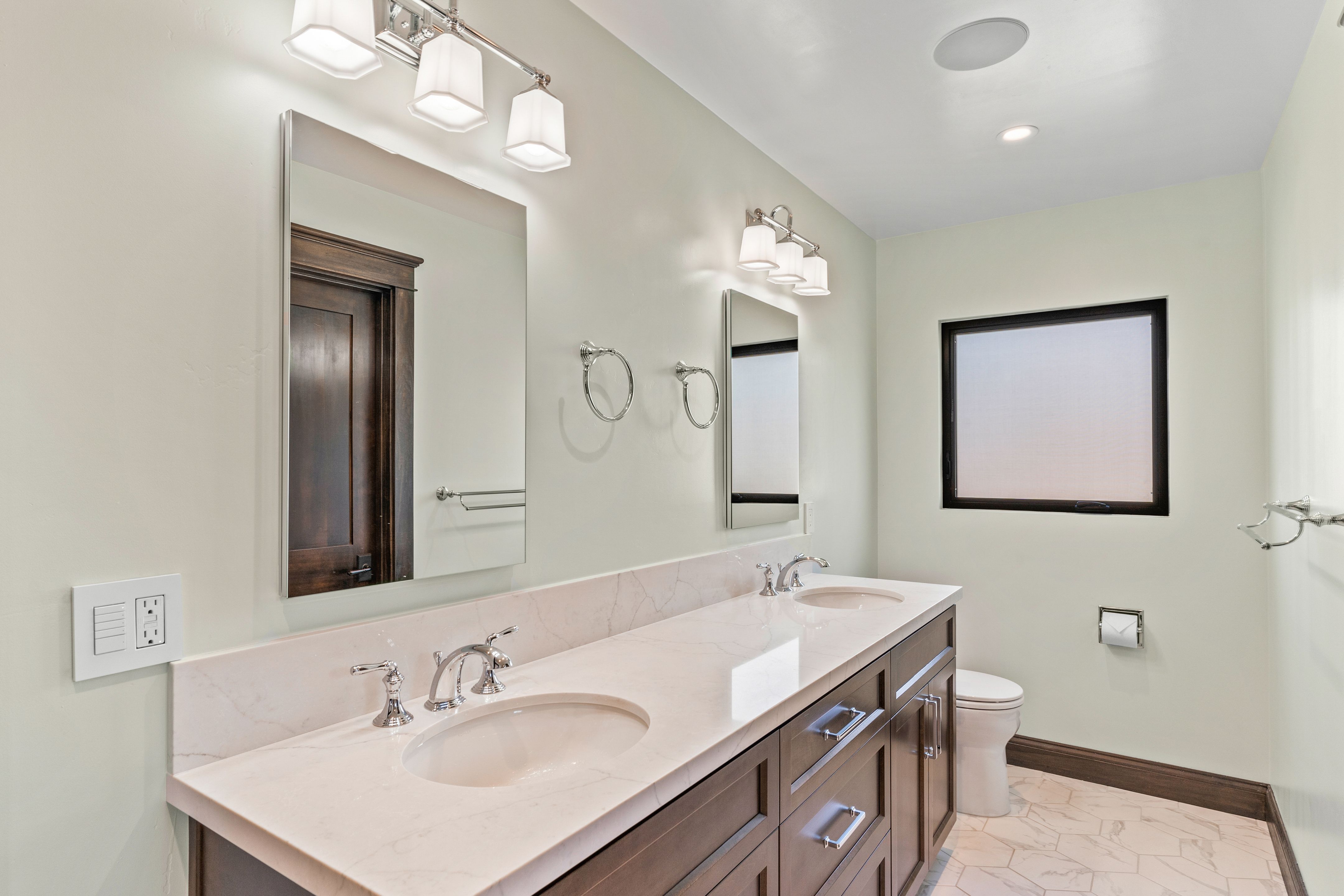 Primary bathroom with double vanity, quartz countertop, chrome fixtures and dark wood trim