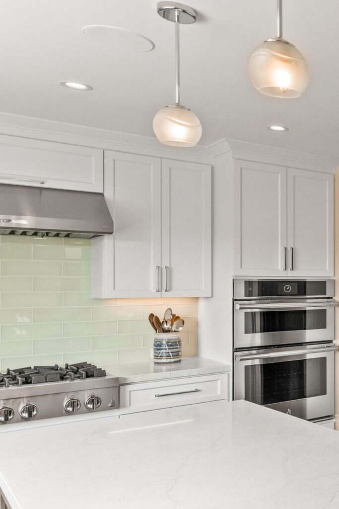 Kitchen island with light countertop, white cabinetry, stainless cooking appliances and glass pendant lights