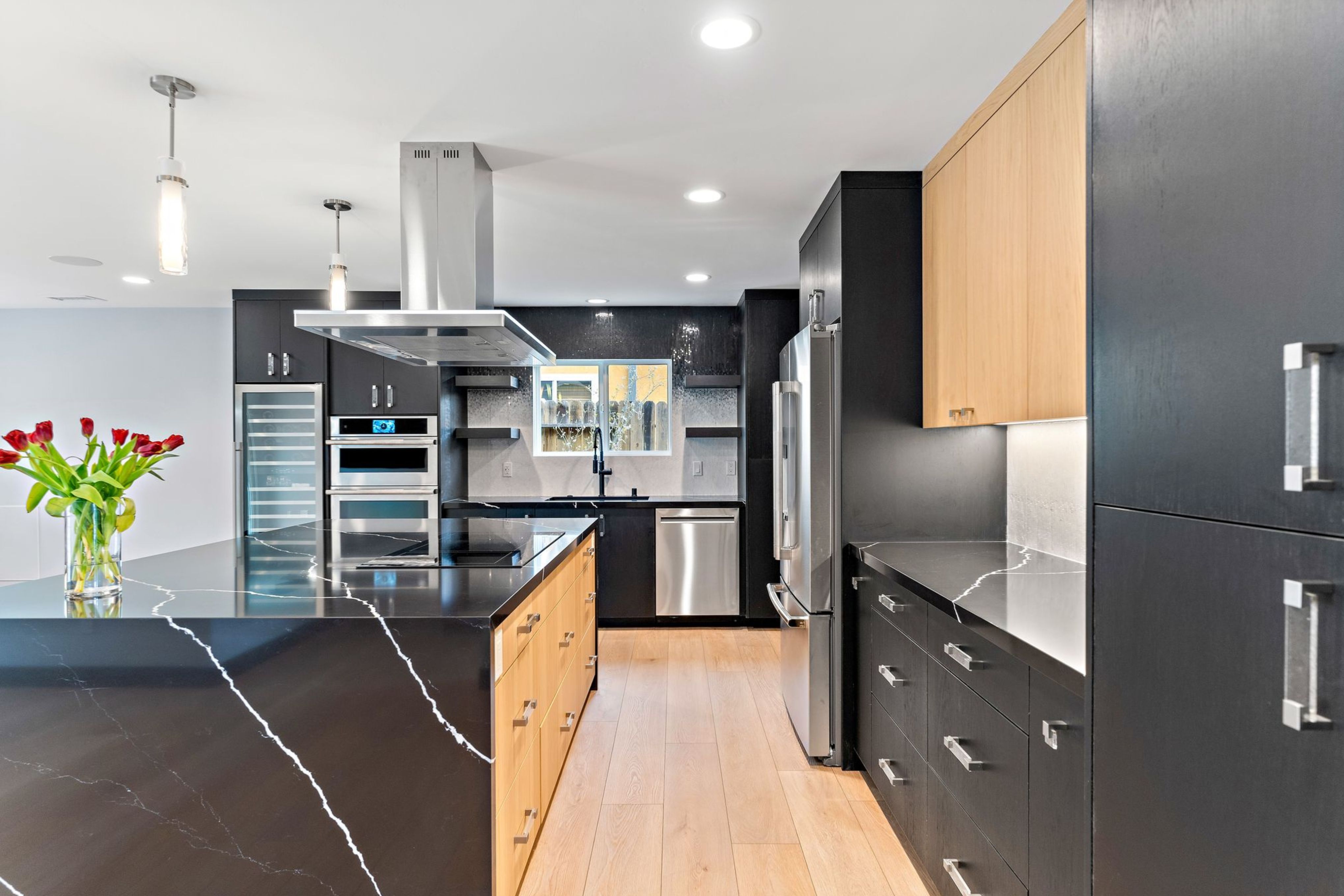 Remodeled kitchen with black and wood cabinetry, veined counters, stainless appliances and wine storage