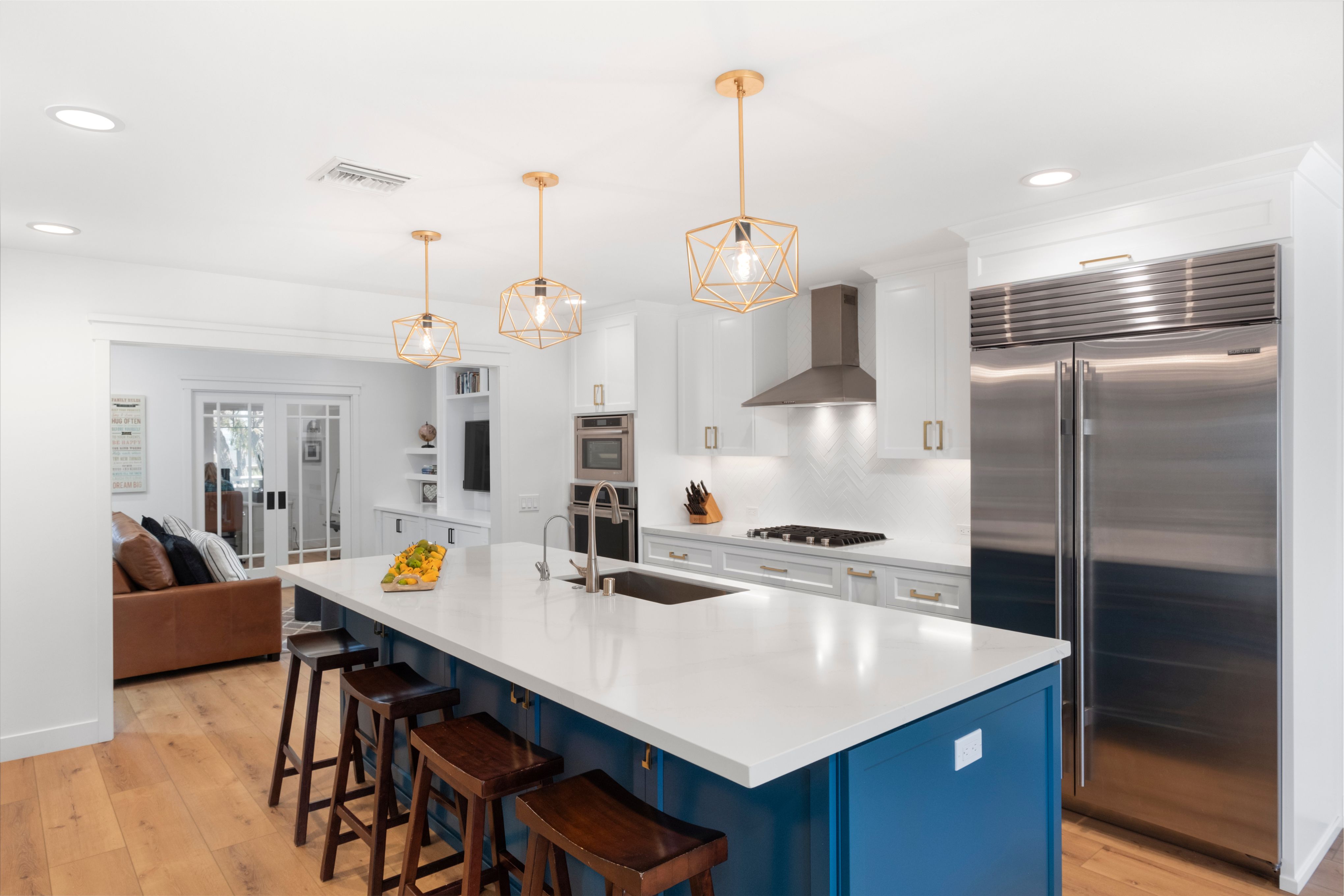 Ocean Beach kitchen with blue island, white quartz counters, brass pendants, white cabinets, and stainless refrigerator.