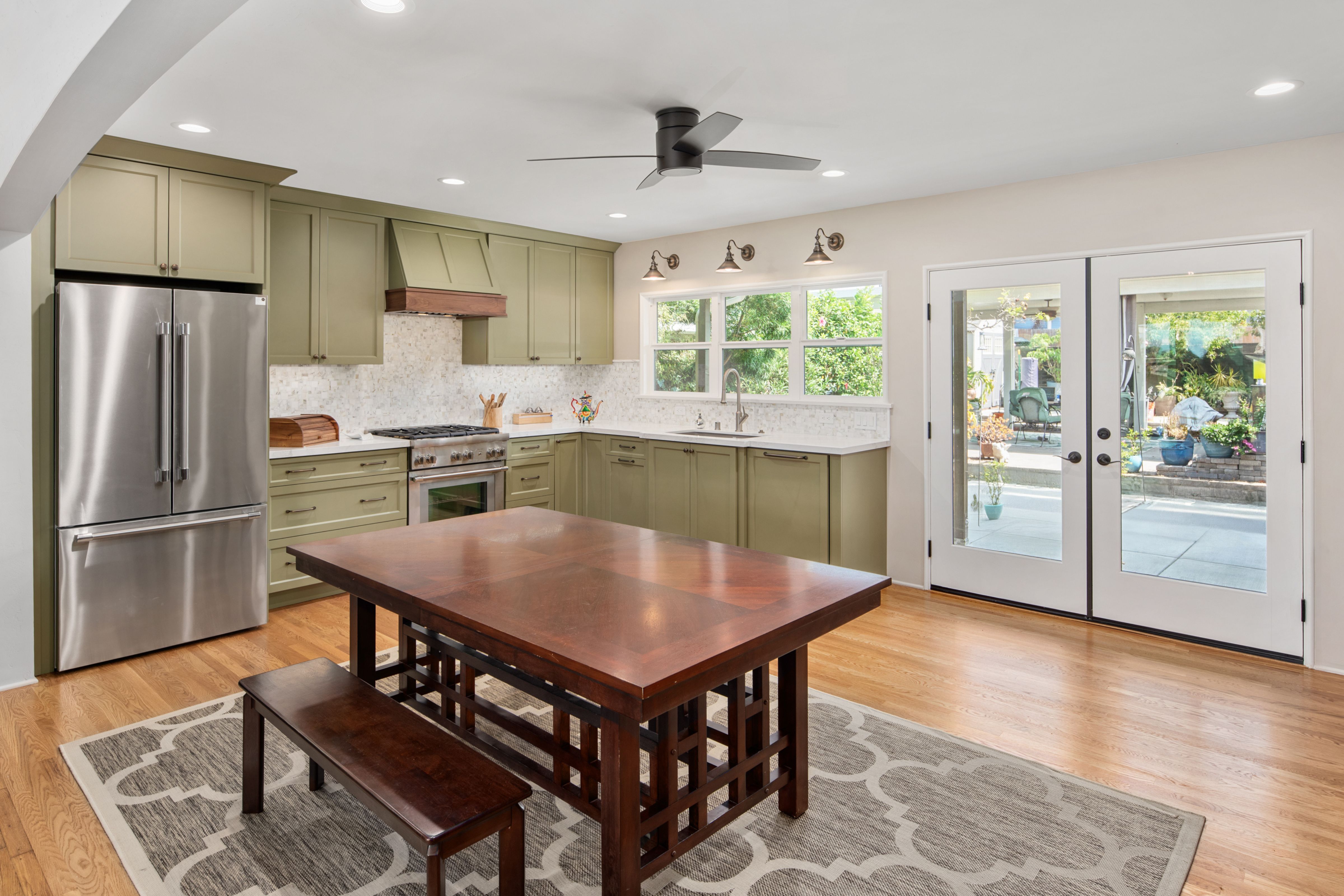 Sage green kitchen with stainless appliances, mosaic backsplash, hardwood floors and glass French doors.