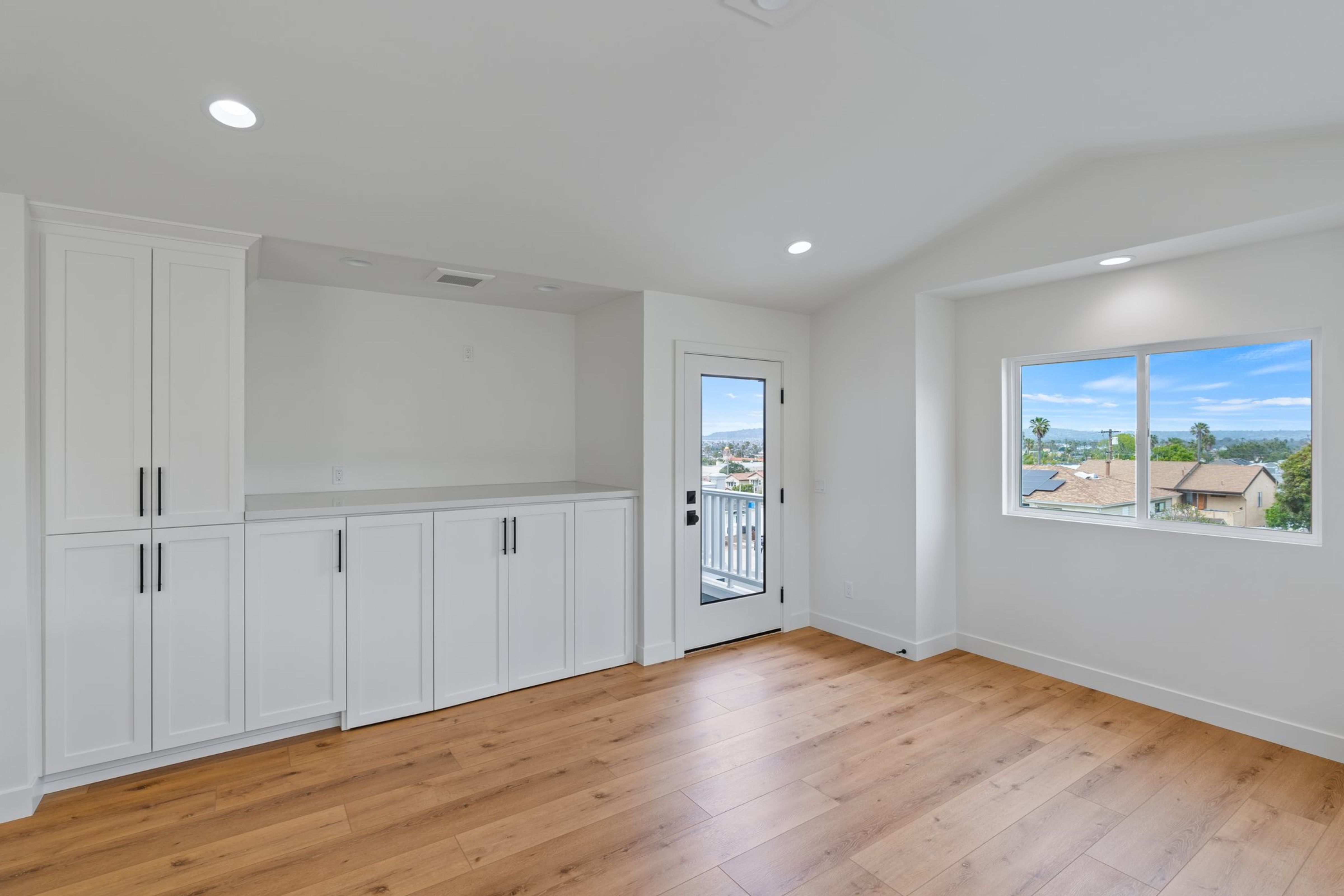 Second-floor room with built-in white cabinetry, wood flooring, large window and door to an exterior deck.