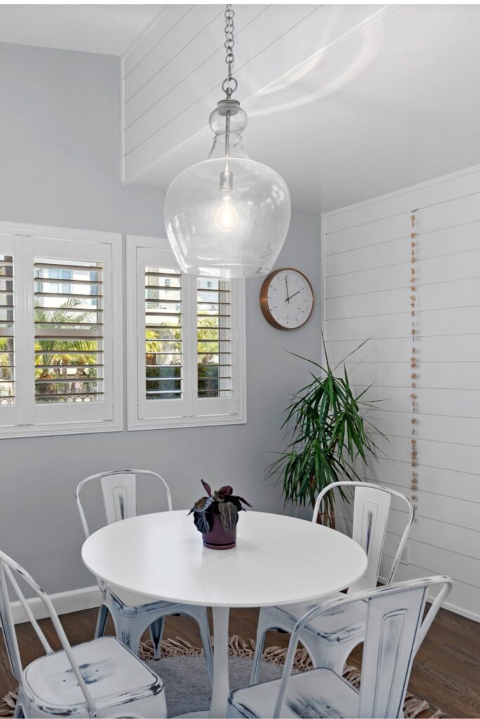 Dining nook with round table, white chairs, plantation shutters, shiplap wall and glass pendant light