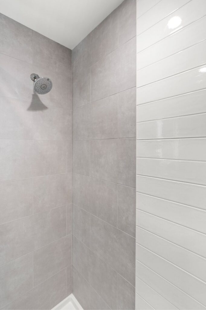 Shower with large-format gray wall tile, white horizontal tile accent and chrome showerhead.