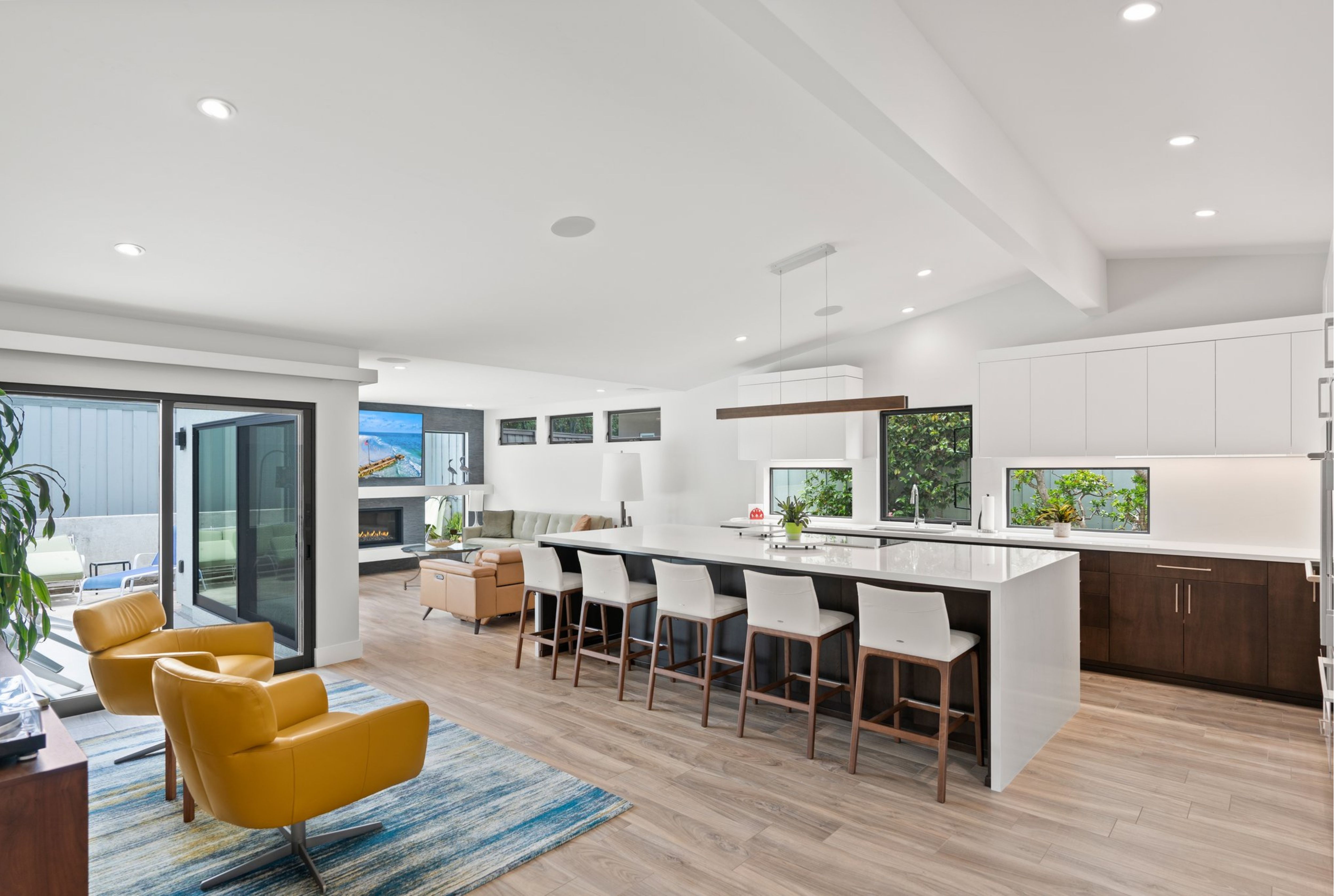 Open kitchen and family room with waterfall island, two-tone cabinetry, black-framed windows and patio doors.