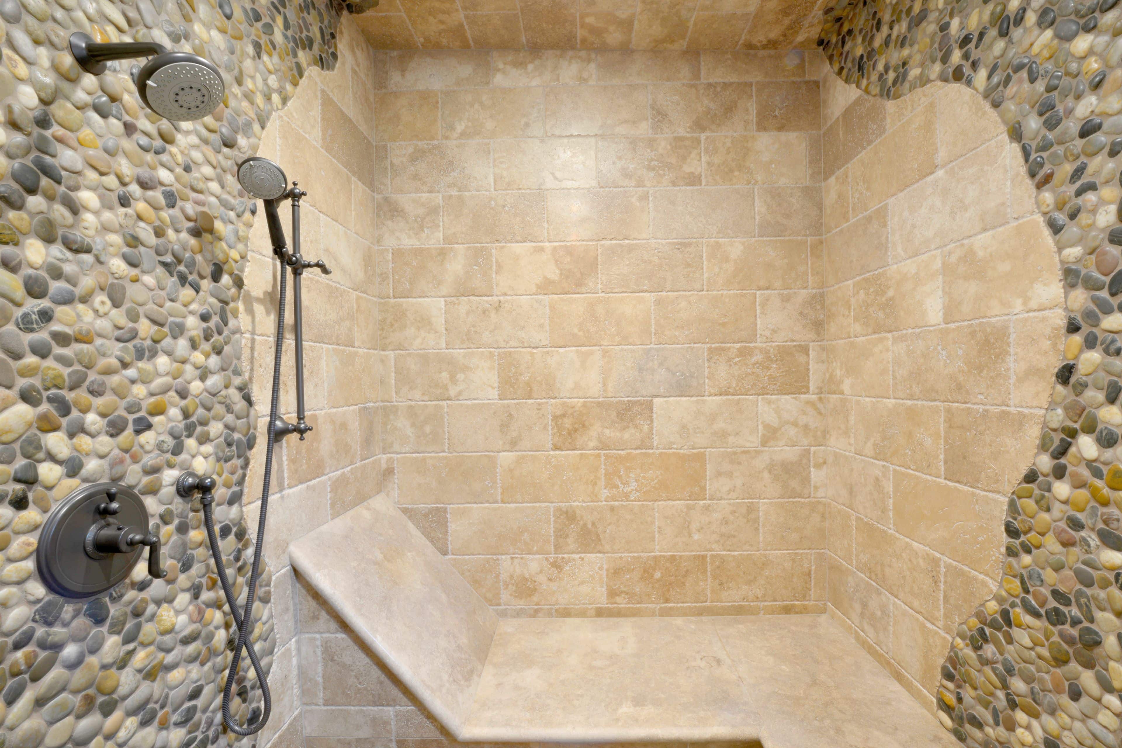Walk-in shower with stone tile walls, pebble accents, built-in bench and dual shower fixtures.