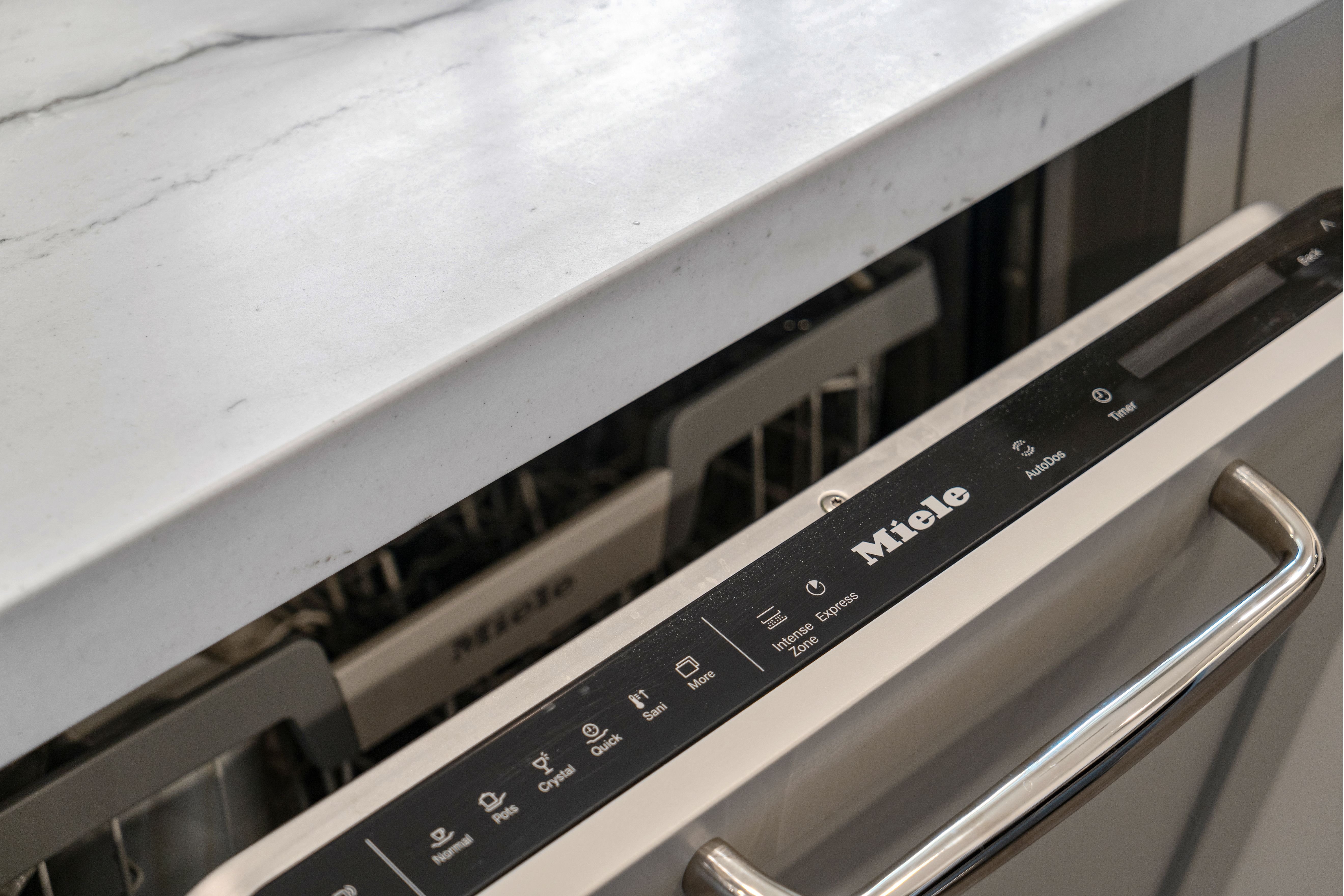 Miele dishwasher integrated beneath a light solid-surface countertop beside painted kitchen cabinetry.