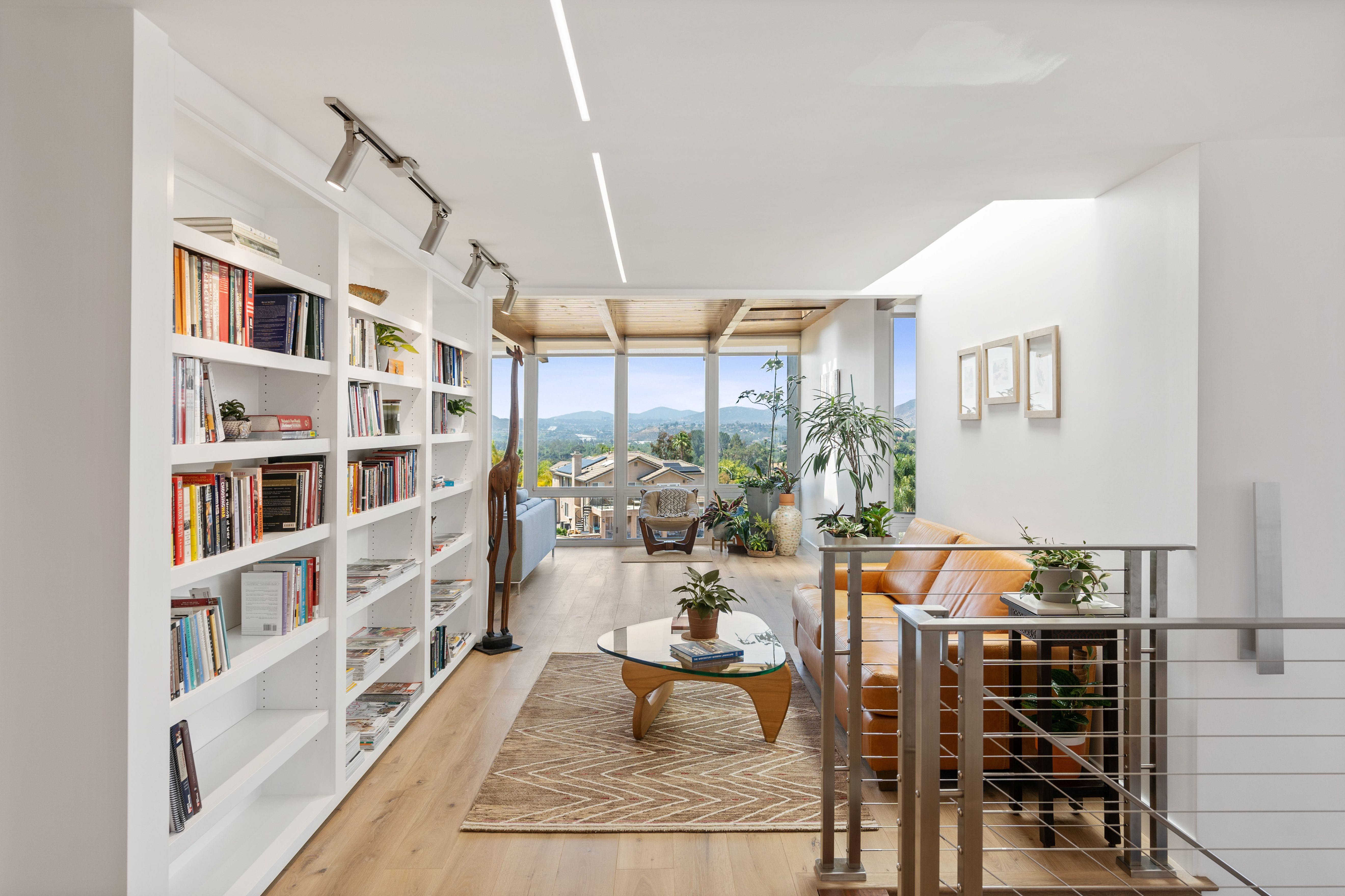 Upper-level sitting area with built-in bookshelves, wood flooring, open railing, track lighting and hillside views