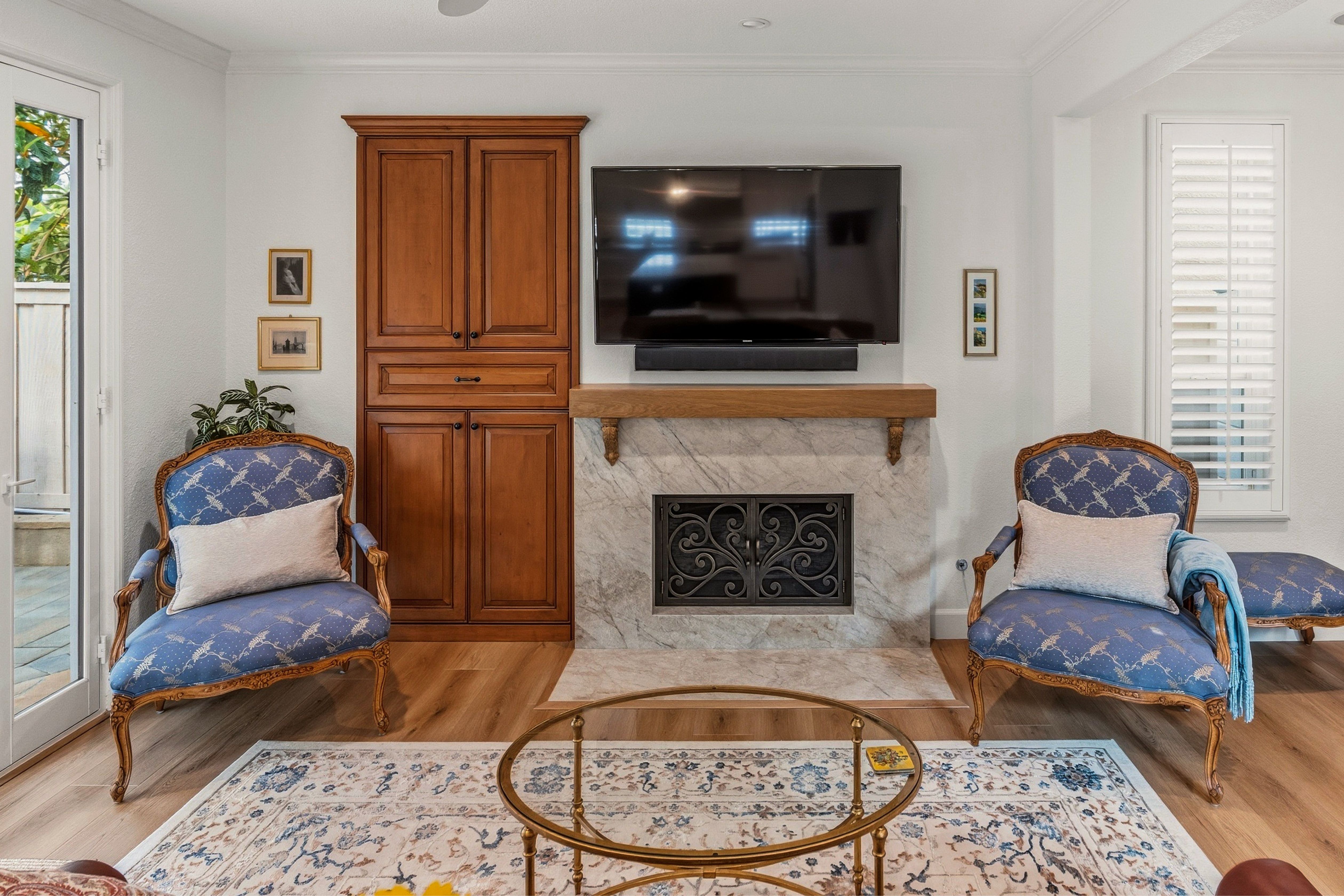 Family room fireplace with a veined stone surround, wood mantel, light flooring and adjacent built-in cabinetry.