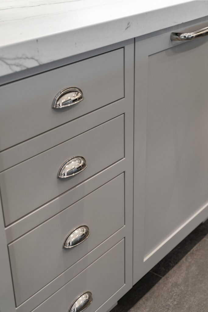 Gray inset kitchen drawers with polished cup pulls beneath a white veined countertop.
