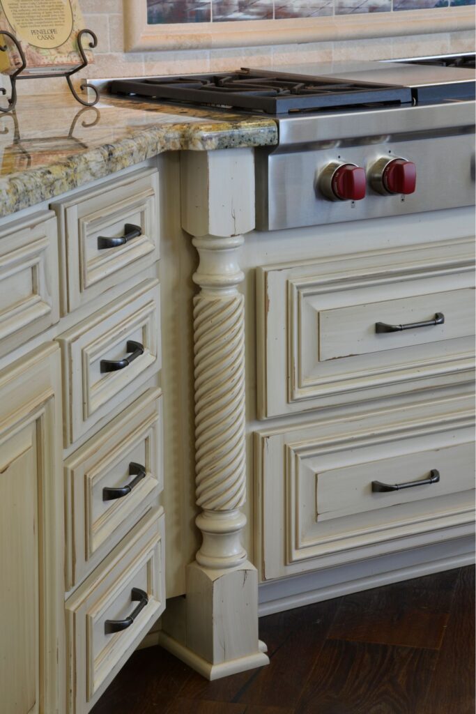 Cream kitchen drawers with dark pulls, twisted column detail, granite counter and stainless range controls.