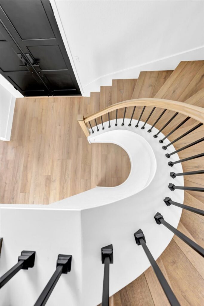 Curved staircase with light wood treads, black metal balusters, rounded wood handrail and black cabinetry below.