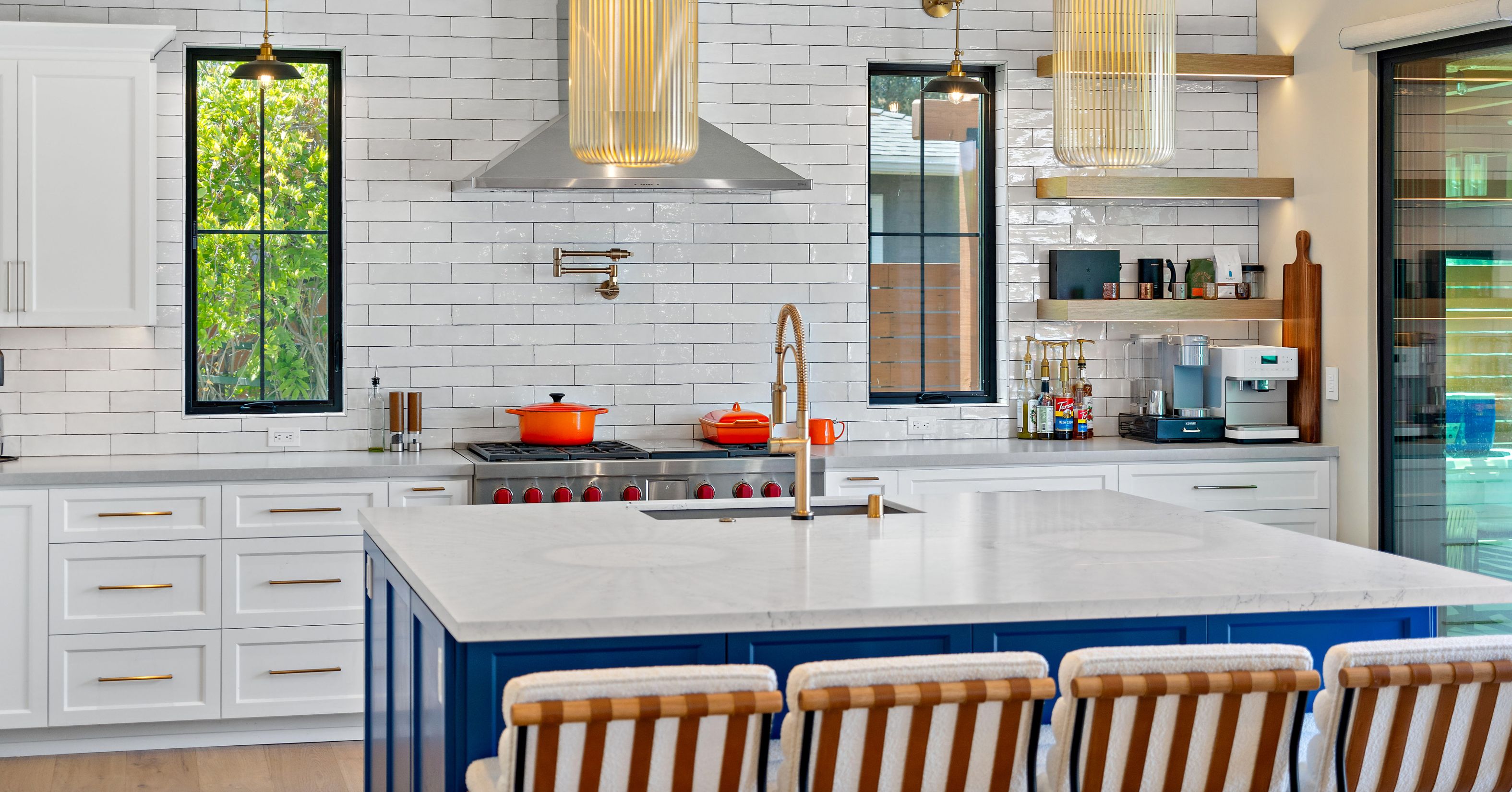 Remodeled kitchen with blue island, white cabinetry, tile wall, range hood, open shelves, and black-framed windows.