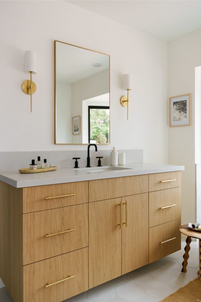 Bathroom with floating light wood vanity, brass hardware and sconces, black faucet and large framed mirror