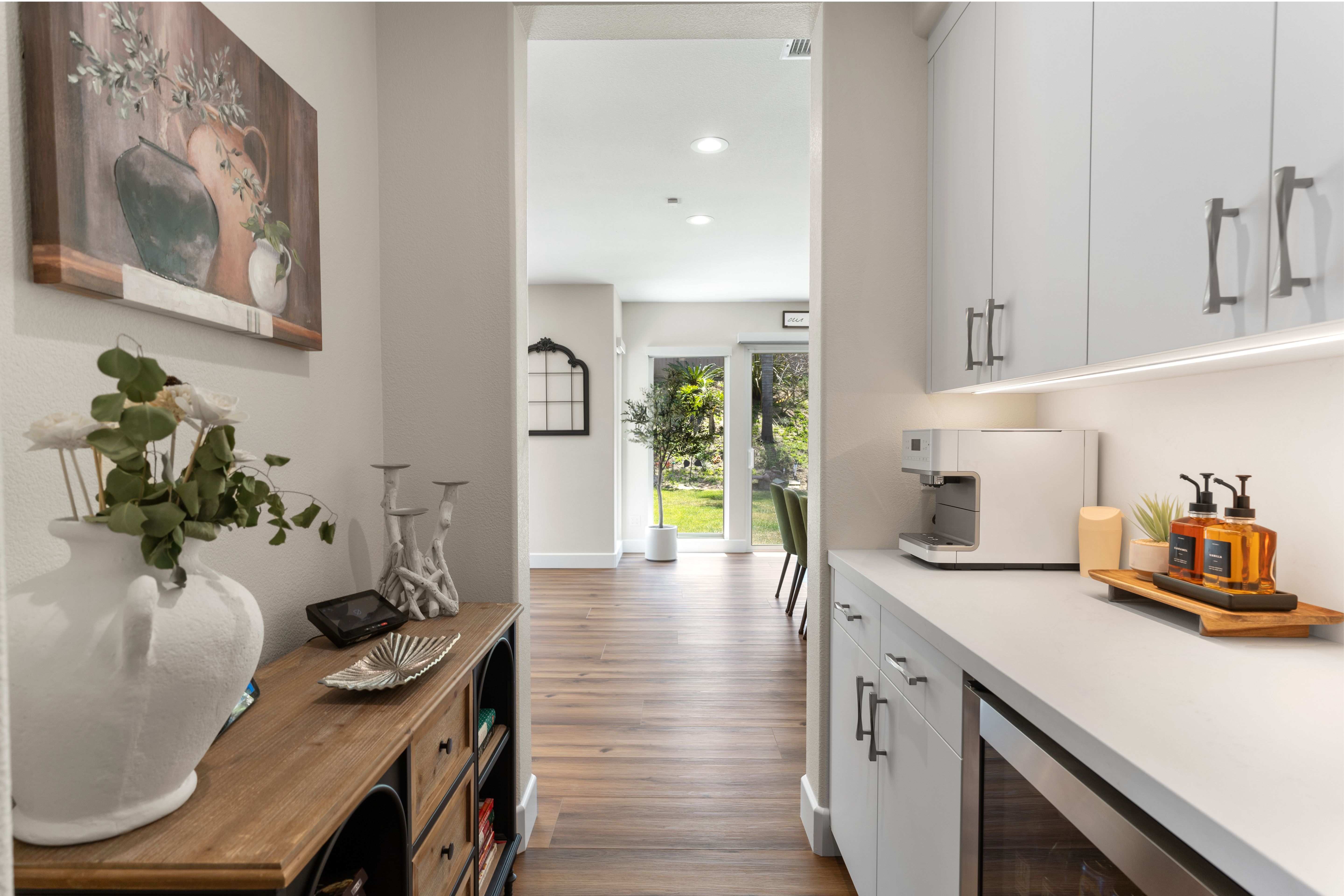 New pantry and coffee area with white cabinetry, long counter, under-cabinet lighting and wood-look flooring.