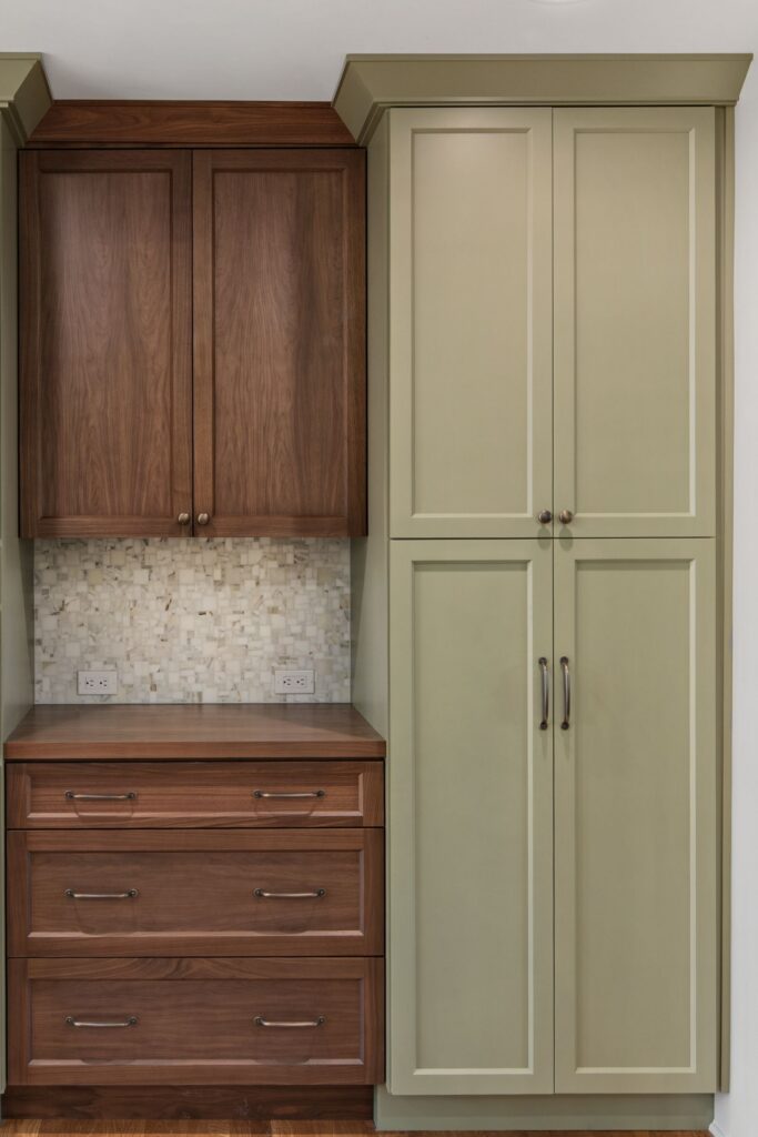 Kitchen storage wall with dark wood cabinetry, sage pantry cabinets, mosaic backsplash, and deep drawers.