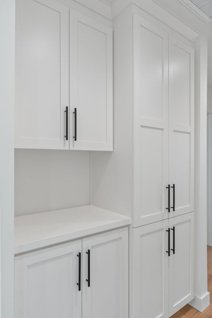 Floor-to-ceiling white built-in cabinetry with shaker doors, black pulls and integrated countertop niche.