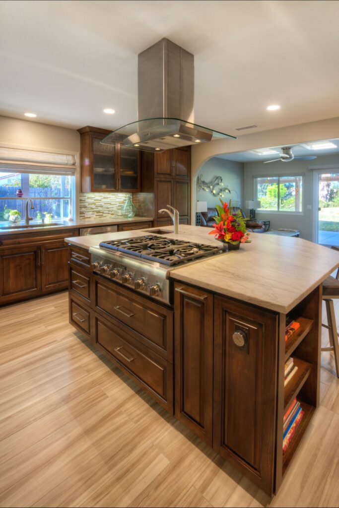 Kitchen island with gas cooktop, prep sink, curved glass hood and dark wood cabinetry opening to the living area.