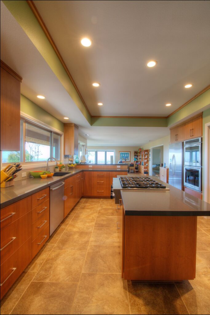 Open kitchen with wood cabinetry, cooktop island, stainless appliances, tile flooring and recessed lighting