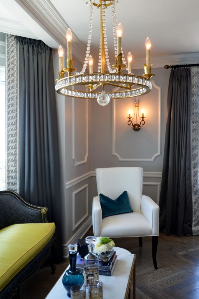 Sitting room with crystal chandelier, decorative wall molding, dark drapery, hardwood floors and upholstered chairs