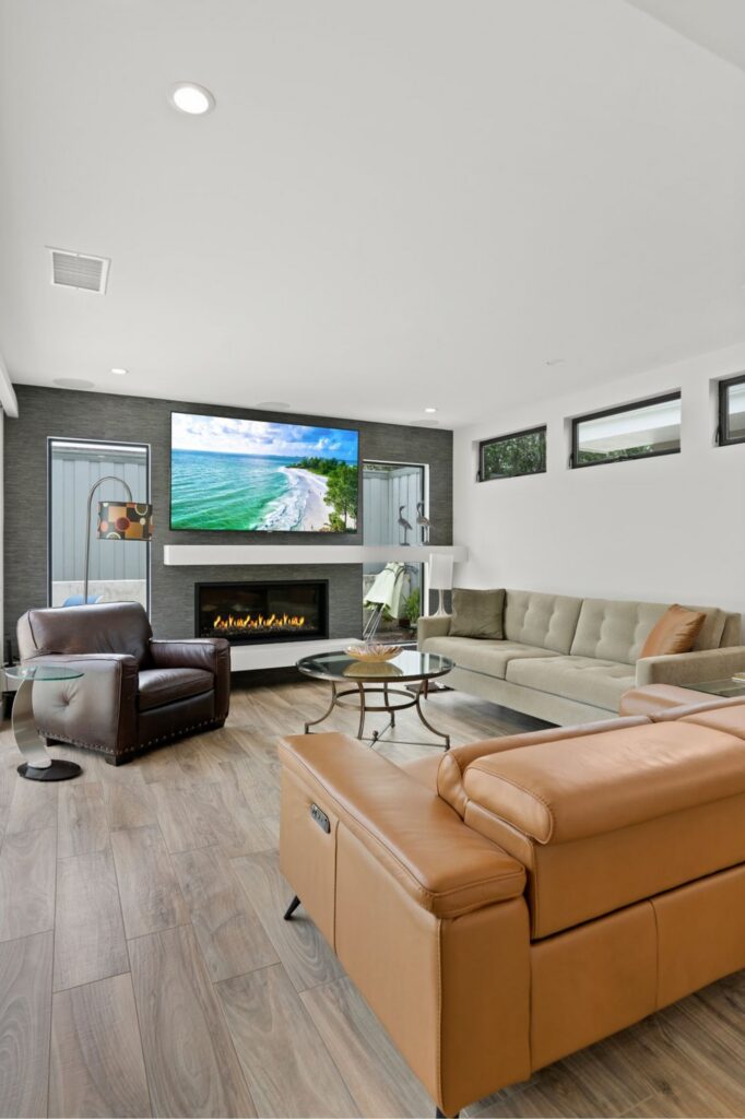 Family room with fireplace, wall-mounted TV, dark accent wall, clerestory windows and wood-look flooring.