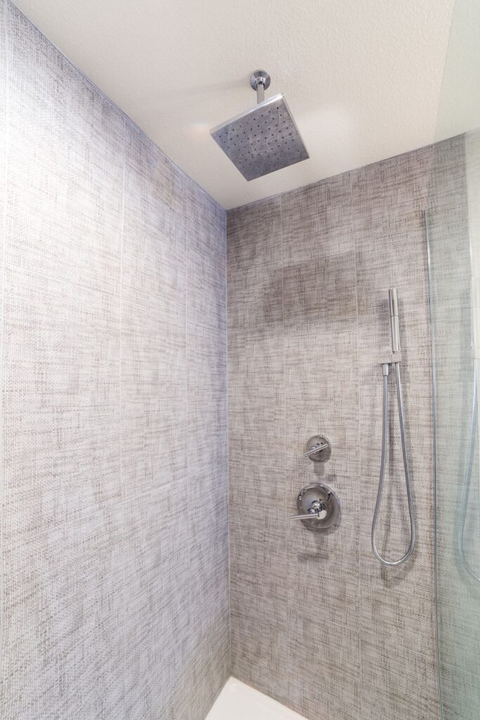 Primary shower with textured gray wall tile, square rain head, handheld sprayer and frameless glass panel.