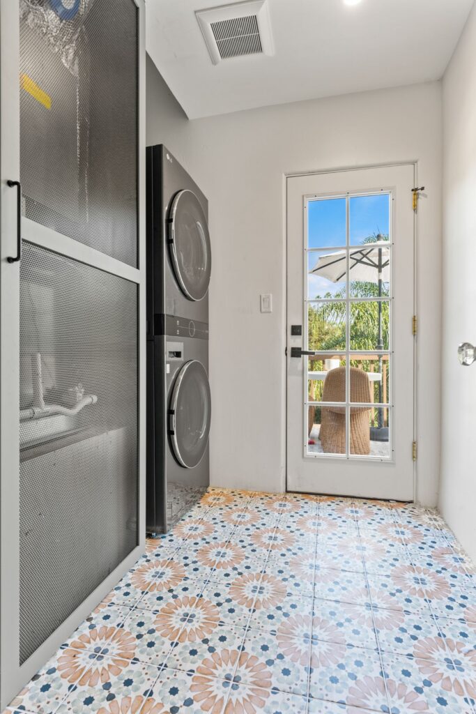 Upstairs laundry and mud room with stacked washer and dryer, patterned tile floor, storage cabinet and glass-paneled door