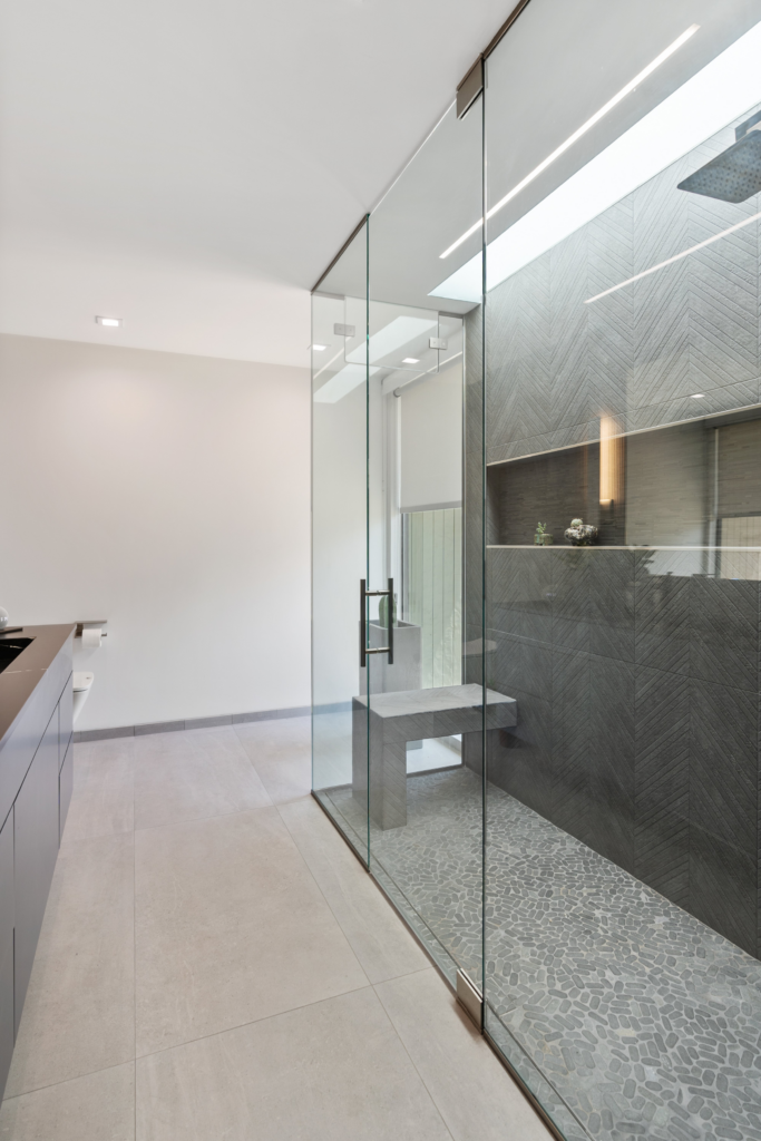 Glass-enclosed bathroom shower with dark chevron wall tile, pebble floor, built-in bench and recessed niche.