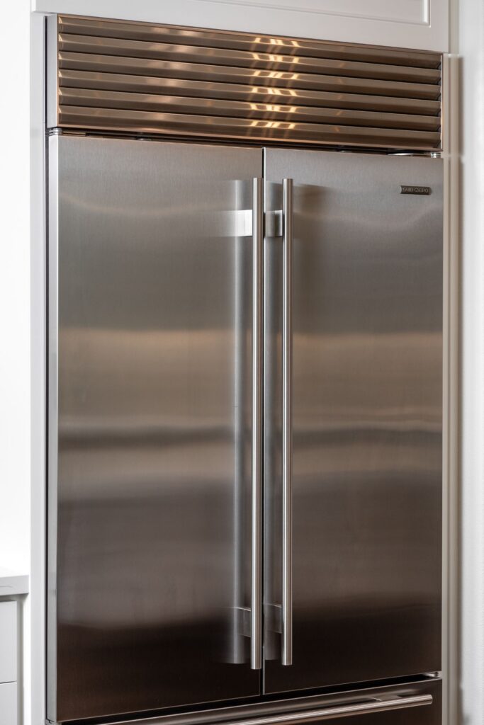 Stainless steel refrigerator integrated between tall white paneled kitchen cabinets.