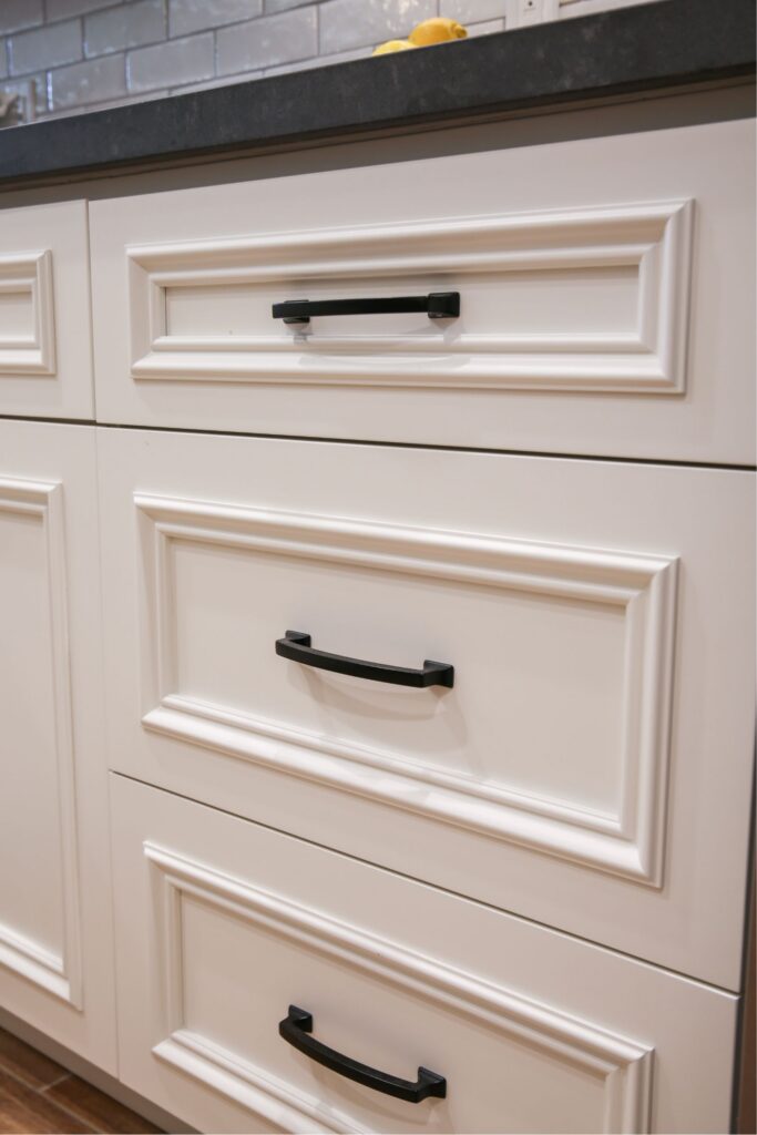 White raised-panel kitchen drawers with black pulls beneath a dark gray countertop and subway tile backsplash