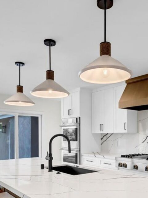 Kitchen island with white veined countertop, black sink and faucet, white cabinetry and three pendant lights.