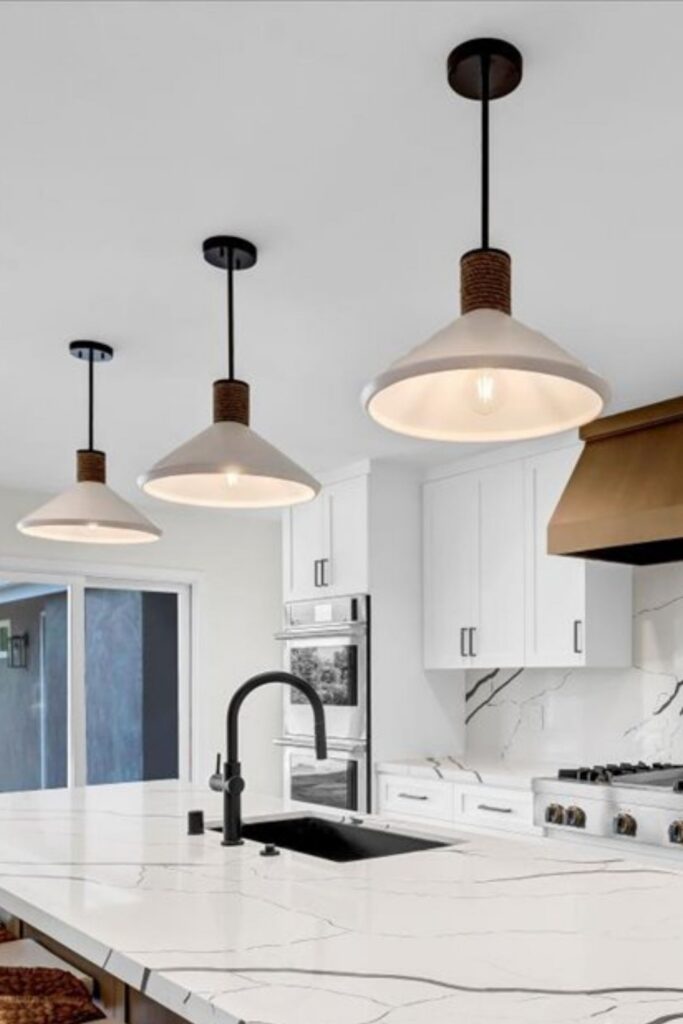 Kitchen island with white veined countertop, black sink and faucet, white cabinetry and three pendant lights.