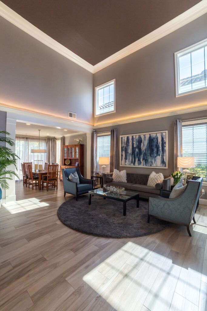 Two-story living room with clerestory windows, cove lighting, gray seating and open connection to the dining room.
