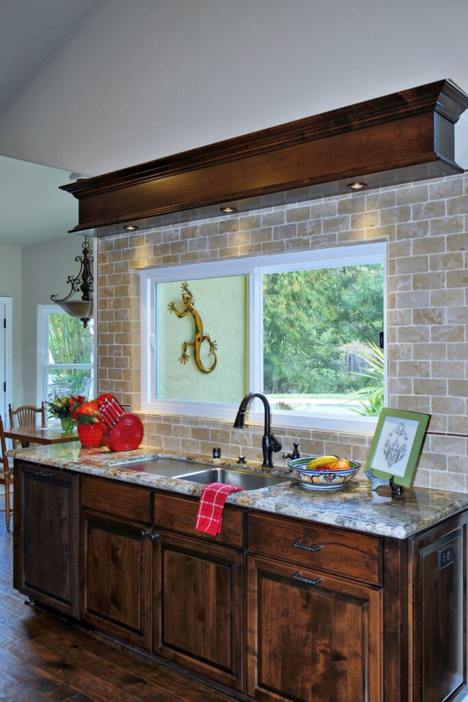 Kitchen sink wall with dark wood cabinetry, granite countertop, stone tile surround and large garden-view window