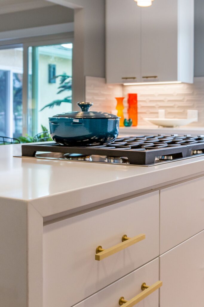 Kitchen island cooktop with white countertop, brass cabinet pulls and dimensional white tile backsplash