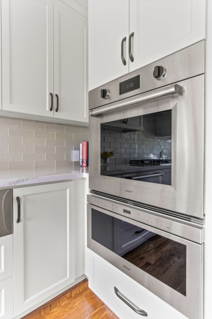 Built-in stainless wall oven and microwave surrounded by white cabinetry with dark hardware.